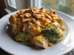 A close-up serving of creamy Chicken Divan featuring chunks of chicken, broccoli florets, and a cheesy sauce topped with crushed cornflakes.