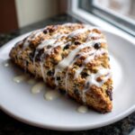 A triangular slice of freshly baked chocolate chip scones drizzled generously with white vanilla glaze.