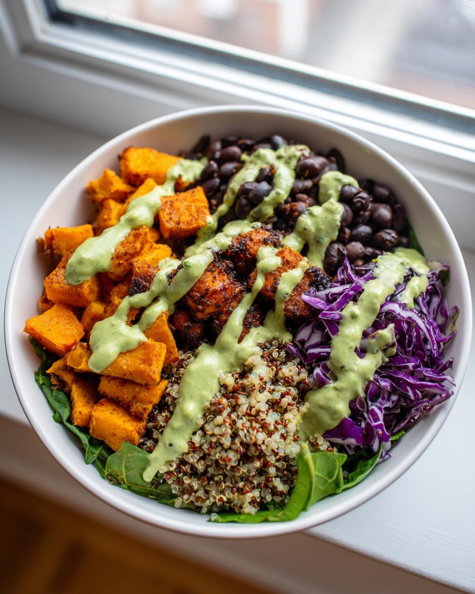A vibrant buddha bowl featuring quinoa, roasted sweet potatoes, black beans, and red cabbage, drizzled with green dressing.
