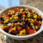Close-up of vibrant cowboy caviar recipe featuring black beans, corn, tomatoes, and red onion in a white bowl.