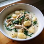 A close-up of a comforting bowl of creamy chicken and spinach gnocchi soup, featuring plump gnocchi dumplings.
