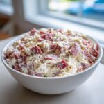 A white bowl filled with creamy, chunky hoagie dip featuring visible pieces of deli meat.