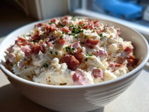 Close-up of a creamy hoagie dip loaded with chunks of ham and topped with fresh green chives.