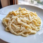Close-up of fettuccine pasta generously coated in creamy olive garden alfredo sauce on a white plate.
