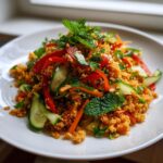 Close-up of a vibrant crispy rice salad mixed with sliced cucumbers, red peppers, and topped with fresh mint leaves.