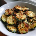 Close-up of crispy, golden brown roasted zucchini slices topped with Parmesan cheese and herbs.
