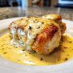 Close-up of pan-seared Dijon chicken breasts smothered in a creamy, yellow sauce and garnished with herbs.