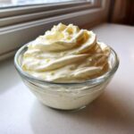 A small glass bowl filled with freshly piped, creamy garlic aioli recipe, garnished with lemon zest.