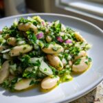A close-up of a vibrant white bean salad tossed with chopped parsley, onion, and a light vinaigrette.