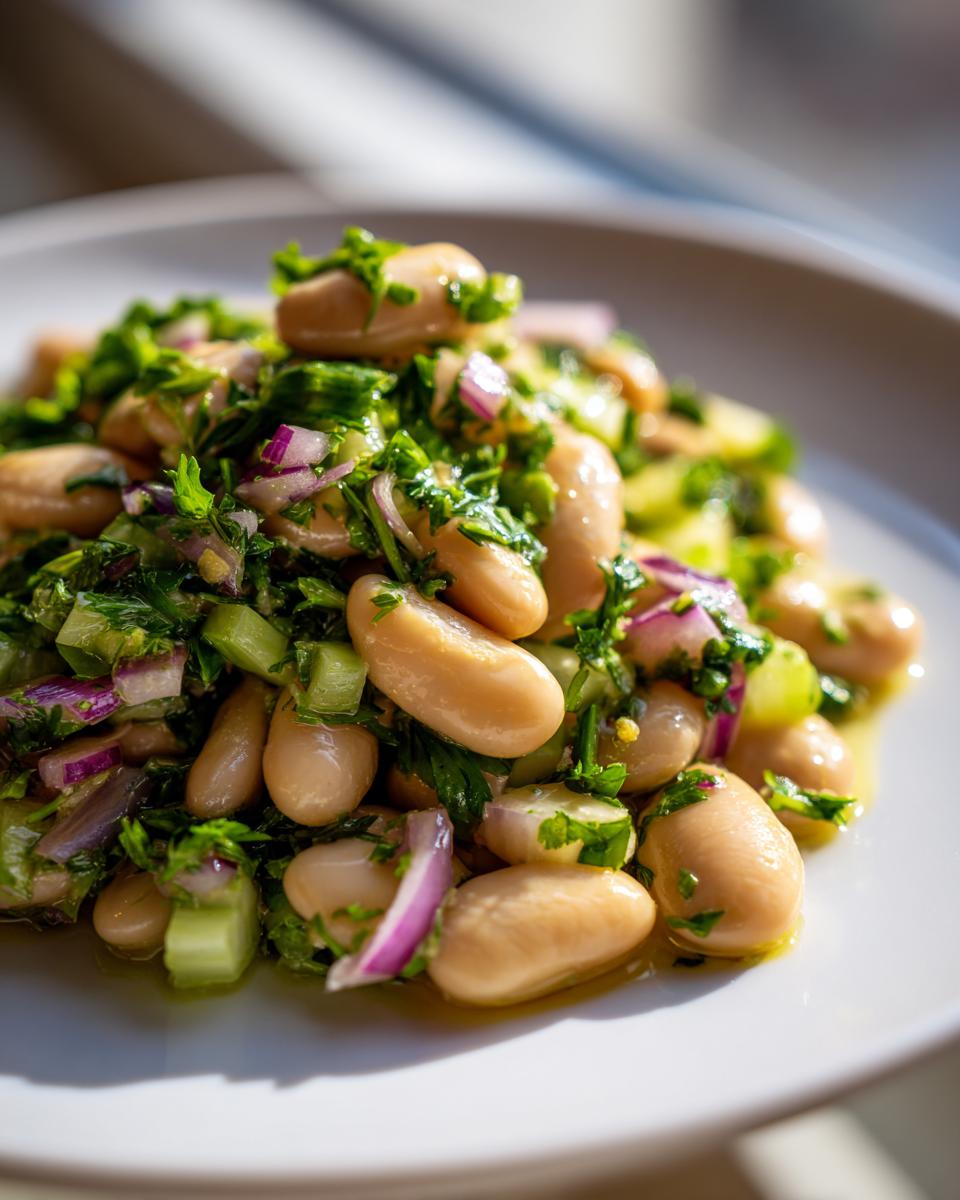 A close-up serving of vibrant white bean salad mixed with chopped red onion, celery, and fresh parsley.