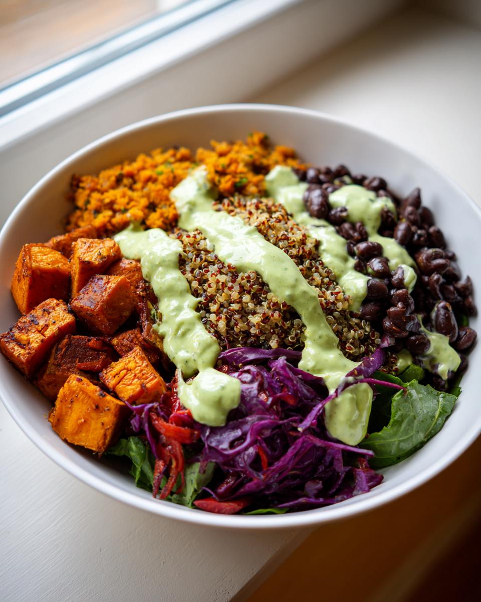 Close-up of a vibrant buddha bowl featuring roasted sweet potatoes, black beans, quinoa, and purple cabbage, drizzled with green dressing.