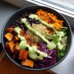 Overhead view of a vibrant buddha bowl featuring roasted sweet potatoes, black beans, quinoa, and shredded red cabbage, drizzled with green dressing.