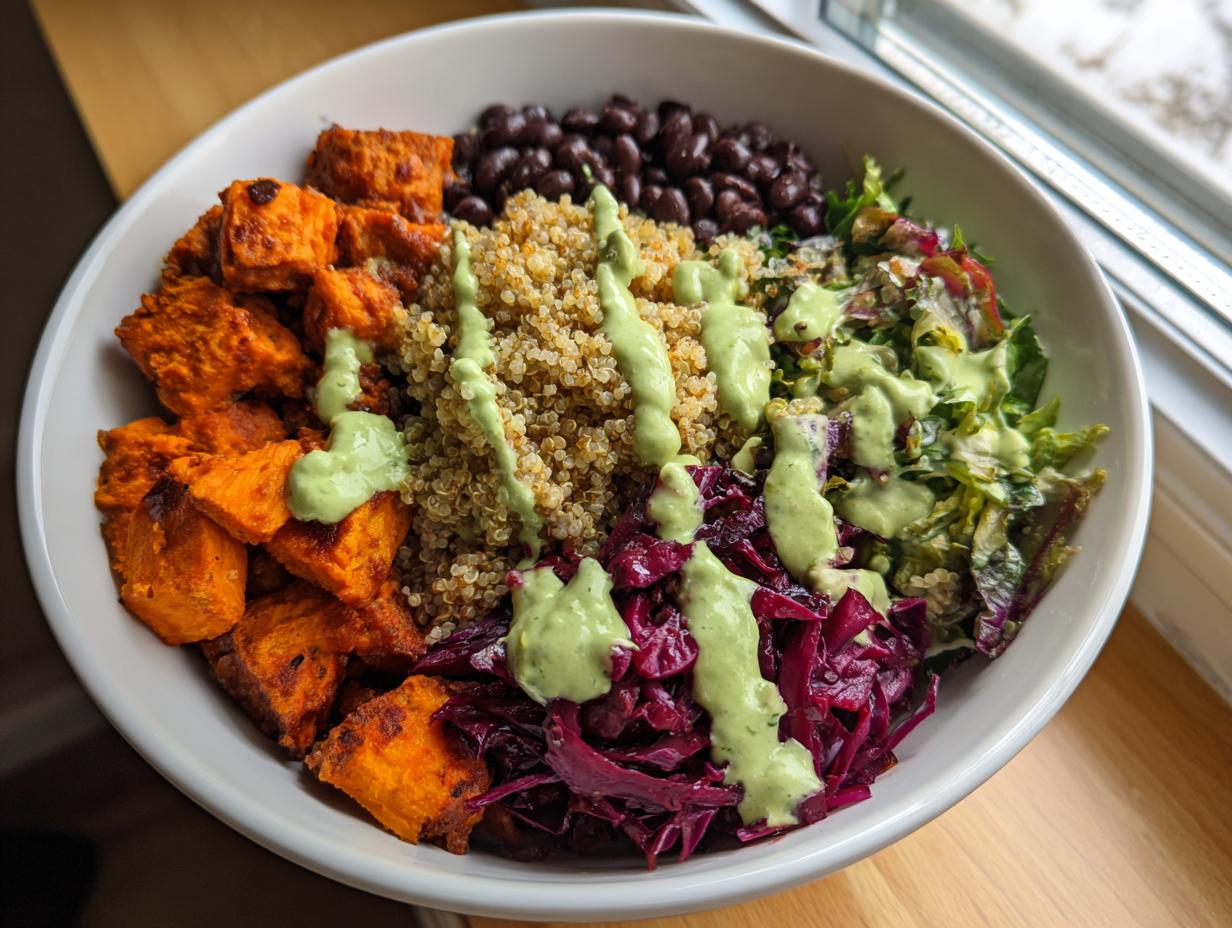 A colorful, fully loaded buddha bowl featuring quinoa, roasted sweet potatoes, black beans, red cabbage, and a creamy green dressing.