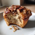 Close-up of a gooey pecan pie muffin with a bite taken out, showing the moist interior and sticky topping.
