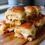 A stack of gooey, cheesy pizza sliders dripping with melted mozzarella and sauce on a wooden board.