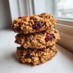 A stack of three thick, oatmeal-based breakfast cookies studded with dried cranberries.