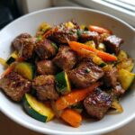 Close-up of juicy hibachi steak bites mixed with sautéed zucchini and carrots in a white bowl.