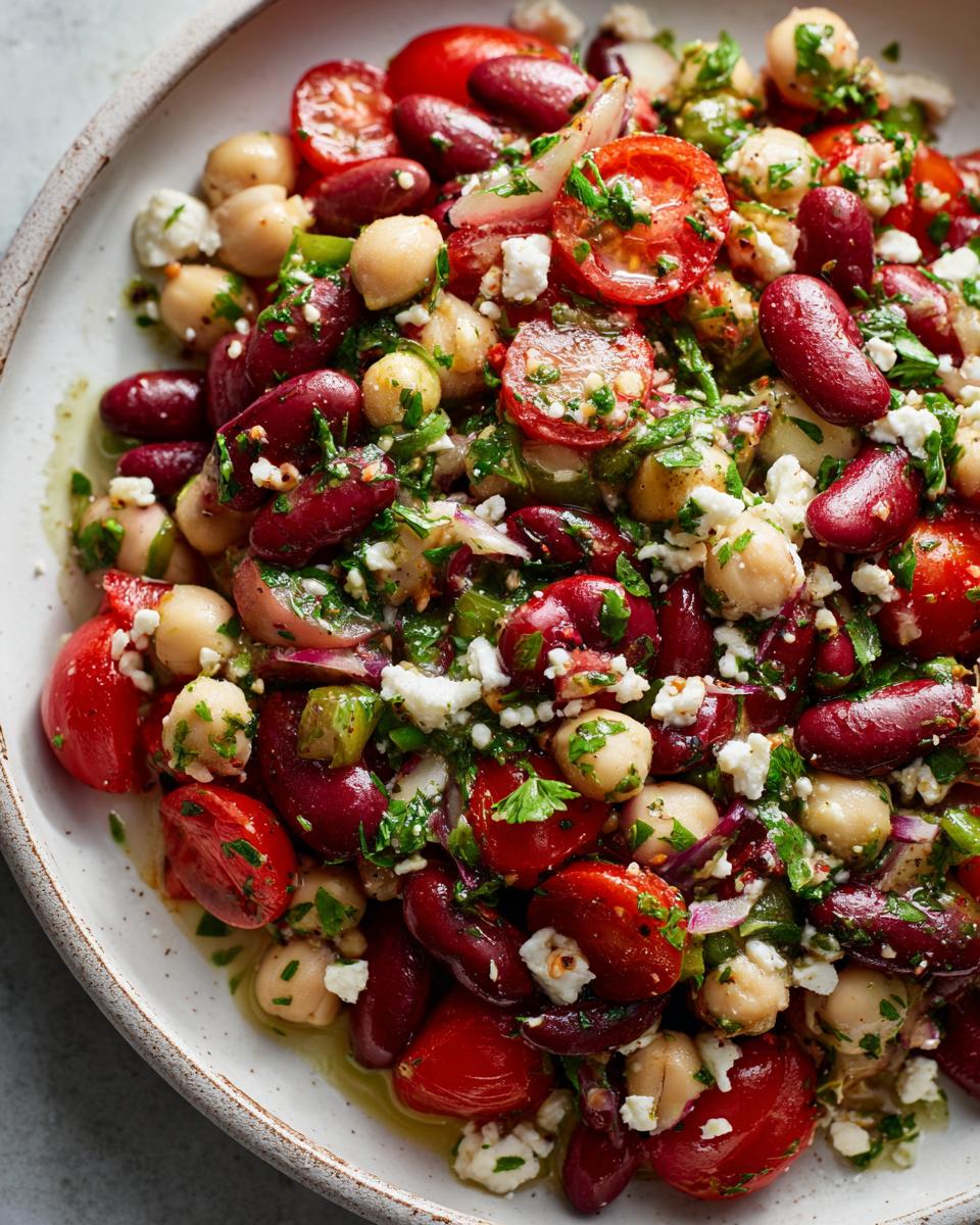 Close-up of a vibrant bean salad featuring kidney beans, chickpeas, cherry tomatoes, and feta cheese.