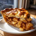 Close-up of a thick slice of homemade apple pie showing flaky, golden crust and rich, spiced apple filling.