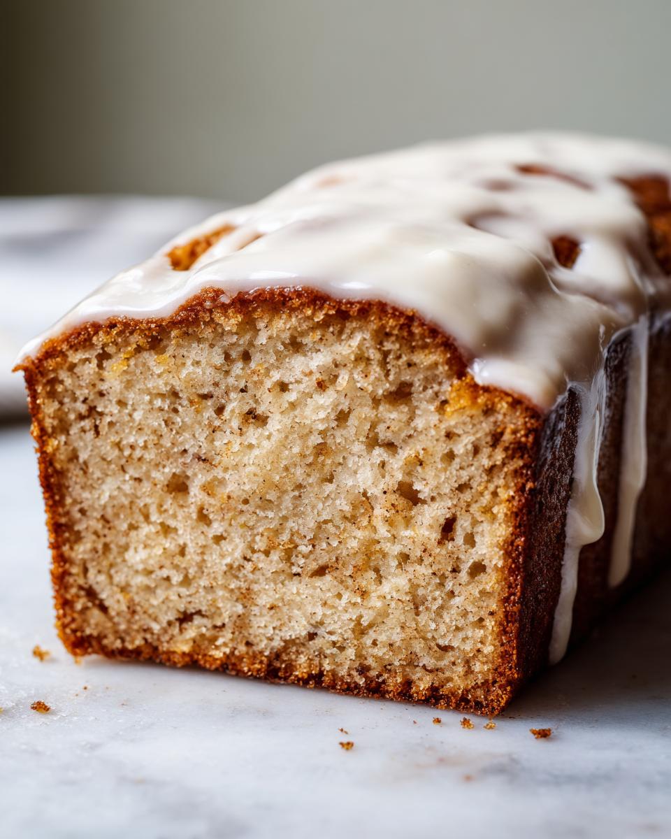 A close-up cross-section of moist eggnog bread topped with a thick white glaze dripping down the side.