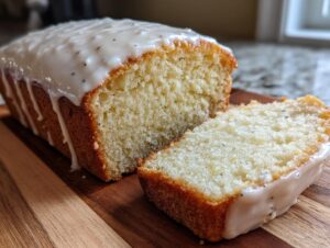 Close-up of moist eggnog bread loaf with a thick vanilla glaze and a slice cut beside it.