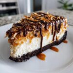 A perfect slice of Samoa Cheesecake with a chocolate crust, creamy filling, caramel, and chocolate drizzle.