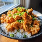 Close-up of crispy bang bang chicken pieces coated in creamy sauce served over white rice and topped with green onions.