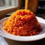 A vibrant mound of perfectly cooked, smoky jollof rice served on a white plate.