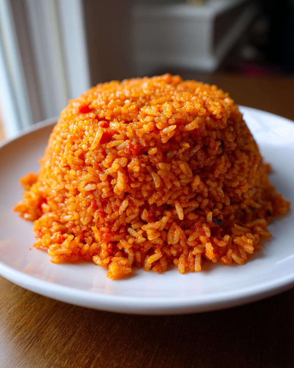 A perfectly molded dome of vibrant orange Jollof rice served on a white plate.