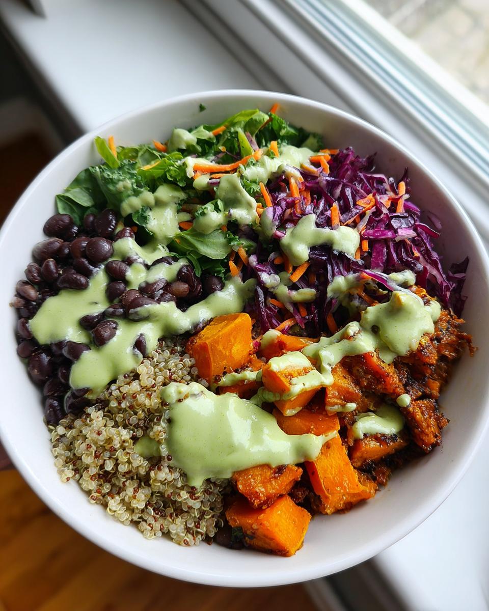Overhead view of a vibrant buddha bowl featuring quinoa, black beans, roasted sweet potatoes, and green dressing.