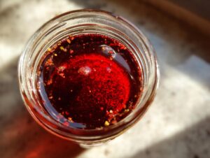 Overhead view of a vibrant red, oil-based salad dressing in a mason jar, showing spices floating on top.