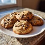 A plate of thick, soft banana bread cookies studded with chocolate chips, catching the morning sunlight.