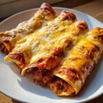 Three freshly baked beef enchiladas covered in melted cheddar and Monterey Jack cheese on a white plate.
