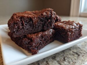 A stack of rich, fudgy black bean brownies with visible chocolate chips on a white rectangular plate.