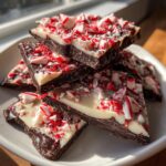 Close-up of stacked pieces of dark and white chocolate peppermint bark topped with crushed candy canes.
