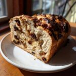 Close-up of a thick slice of soft raisin bread, showing the rich interior filled with plump raisins.