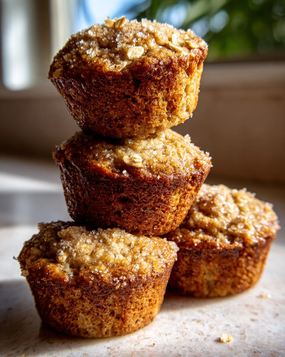 A stack of three golden brown banana oatmeal muffins topped with coarse sugar and oats, beautifully lit.
