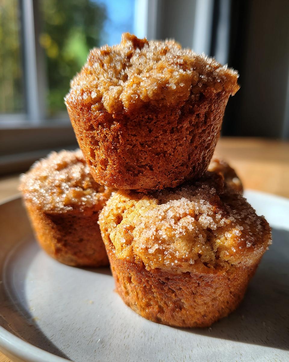 Three golden brown banana oatmeal muffins stacked on a plate, topped with sparkling sugar crystals.