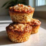 Three golden brown banana oatmeal muffins stacked, featuring a sparkling sugar crust topping.
