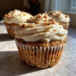 A close-up of a freshly baked banana walnut cupcake topped with thick cream cheese frosting and chopped walnuts.