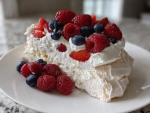 A generous slice of berry pavlova featuring a crisp meringue base, whipped cream, and topped with fresh raspberries, blueberries, and strawberries.