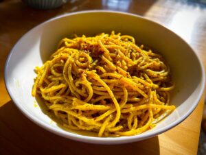 A close-up of vibrant yellow black pepper turmeric cauliflower and garlic noodles served in a white bowl.