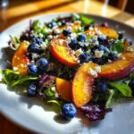 Close-up of a vibrant blueberry peach feta salad featuring fresh greens, sliced peaches, blueberries, and crumbled feta cheese.