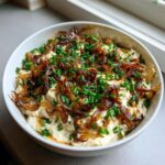 A white bowl filled with creamy caramelized french onion dip, topped generously with dark caramelized onions and fresh green chives.