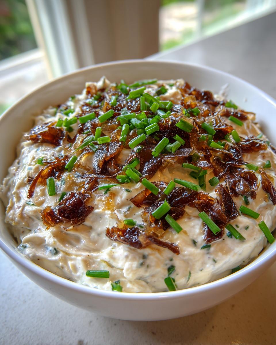 Close-up of a creamy caramelized french onion dip topped generously with dark caramelized onions and fresh green chives.