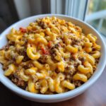 A close-up of a white bowl filled with creamy, cheesy cheeseburger pasta mixed with ground beef and melted cheddar.
