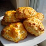 A stack of five golden brown keto protein breakfast biscuits topped with melted cheddar cheese on a white plate.