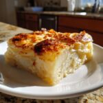 A thick, cheesy slice of scalloped potatoes recipe with a golden-brown, bubbly top, served on a white plate.