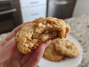 A hand holding a half-eaten, chewy cinnamon toast crunch cookies, showing the soft, gooey interior.