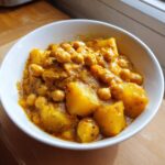 Close-up of a white bowl filled with vibrant yellow chickpea and potato curry.